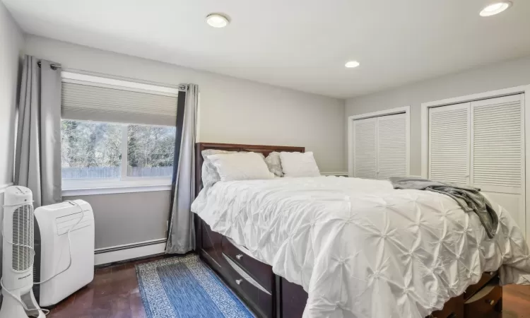 Bedroom with dark wood finished floors, recessed lighting, multiple closets, and a baseboard radiator