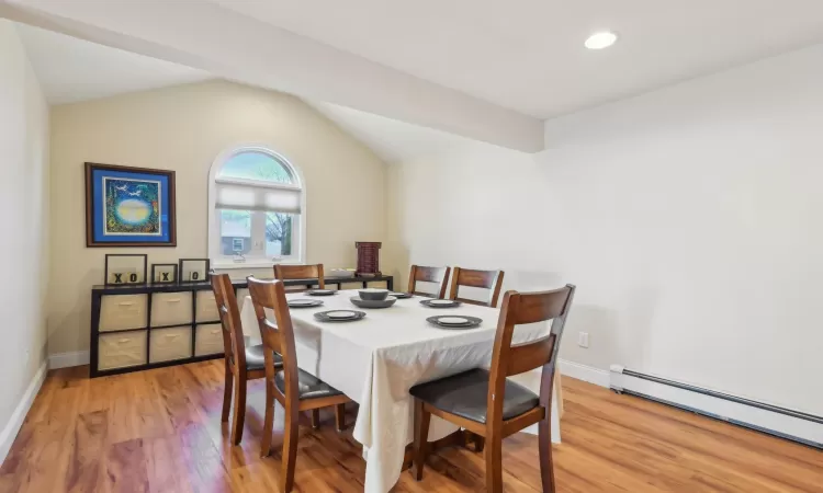 Dining space with light wood-type flooring, a baseboard heating unit, baseboards, and vaulted ceiling