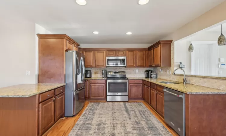 Kitchen with decorative backsplash, light wood-style flooring, appliances with stainless steel finishes, an island with seating