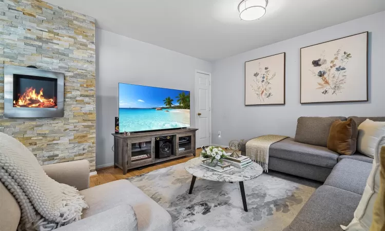 Living area featuring a stone fireplace, wood finished floors, and baseboards