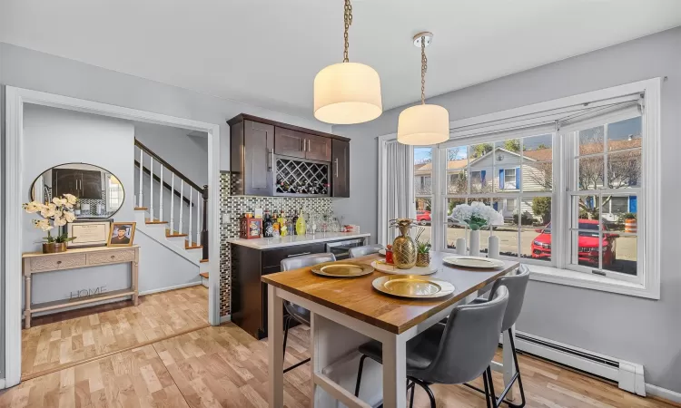 Dining space with stairs, light wood-style flooring, indoor bar, and a baseboard radiator