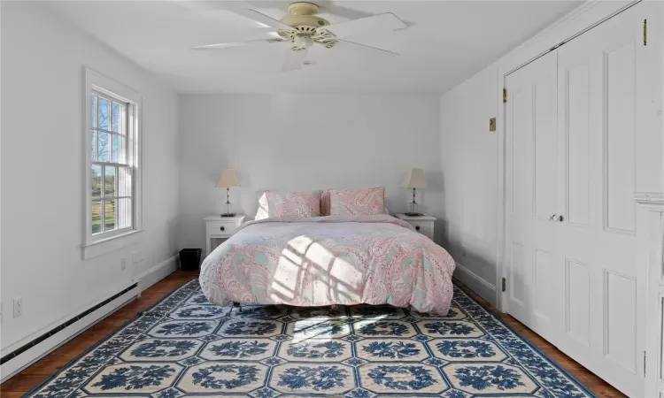 Bedroom featuring a baseboard heating unit, baseboards, wood finished floors, and a ceiling fan