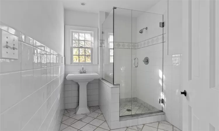 Bathroom with marble finish floor, a stall shower, and tile walls