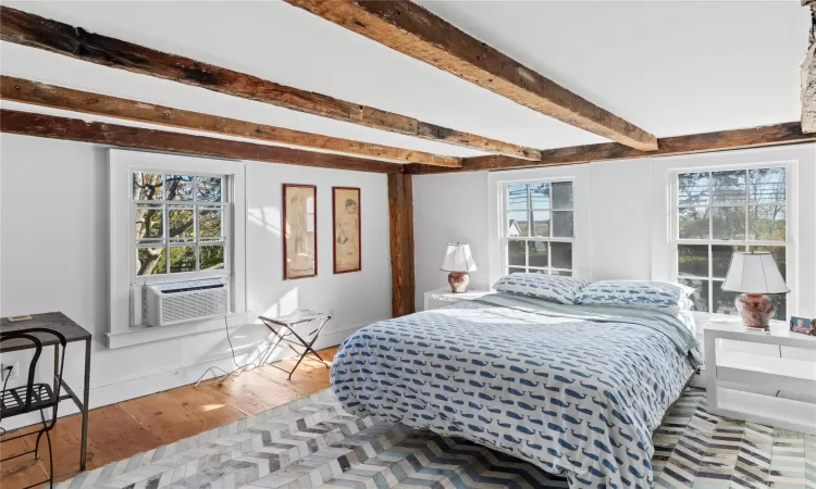 Bedroom with beamed ceiling, cooling unit, wood finished floors, and baseboards