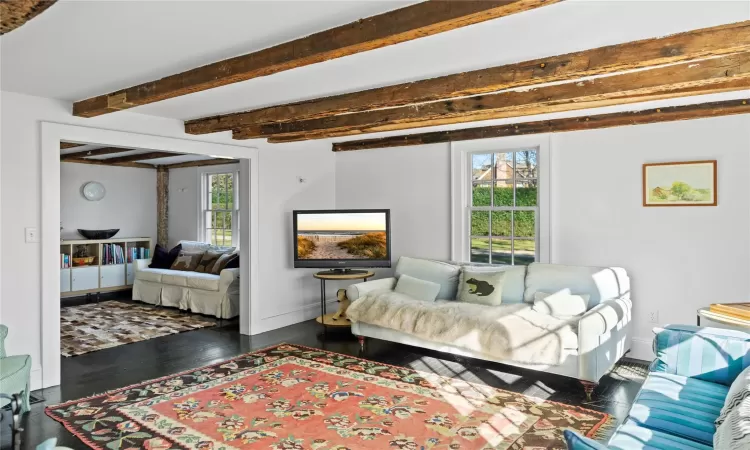 Living area featuring baseboards, beam ceiling, a healthy amount of sunlight, and dark wood finished floors