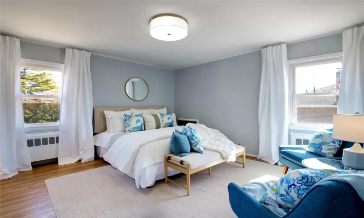 Bedroom featuring multiple windows, radiator heating unit, and wood finished floors