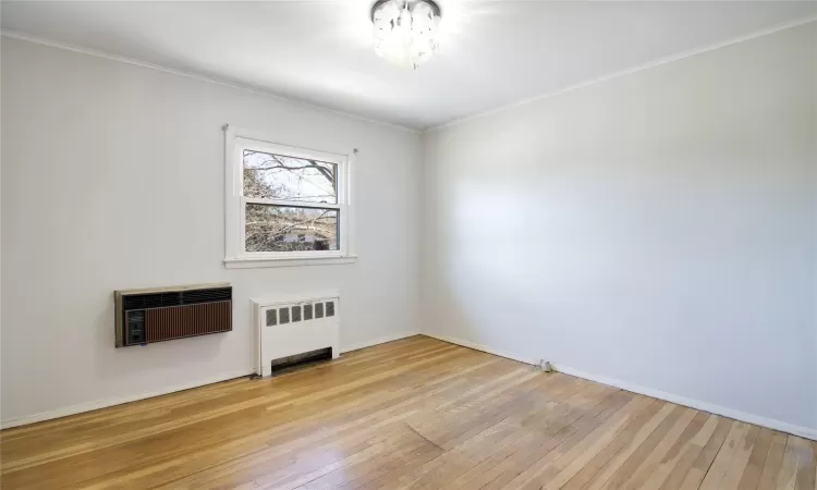 Empty room with heating unit, crown molding, radiator, and wood-type flooring