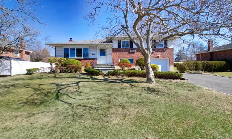 Tri-level home with a front yard, fence, a garage, aphalt driveway, and brick siding