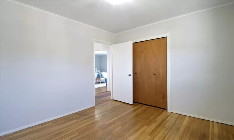 Unfurnished bedroom featuring a closet, light wood-style flooring, baseboards, and ornamental molding