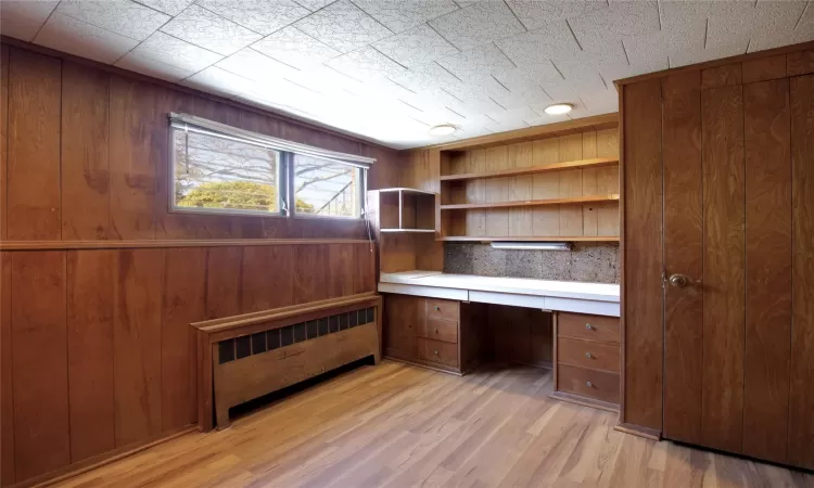 Unfurnished office featuring built in desk, wood walls, and light wood-type flooring