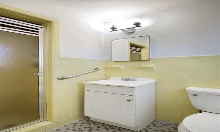 Full bathroom featuring tile walls, toilet, a wainscoted wall, and a shower stall