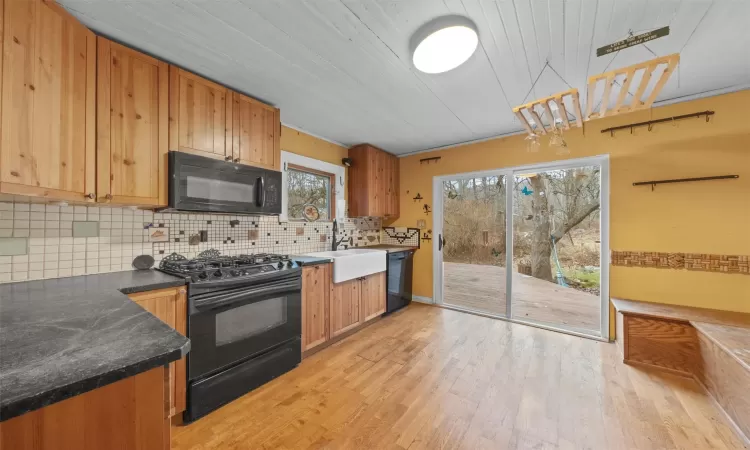 Kitchen with a sink, decorative backsplash, black appliances, dark countertops, and light wood-type flooring