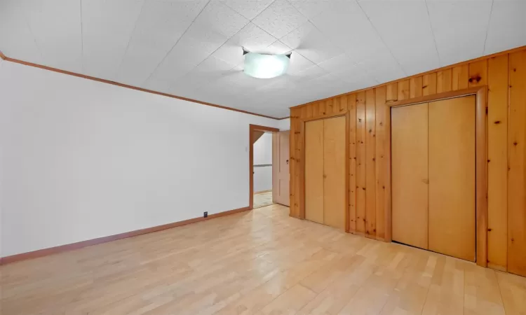 Unfurnished bedroom with wood finished floors, baseboards, wood walls, and ornamental molding