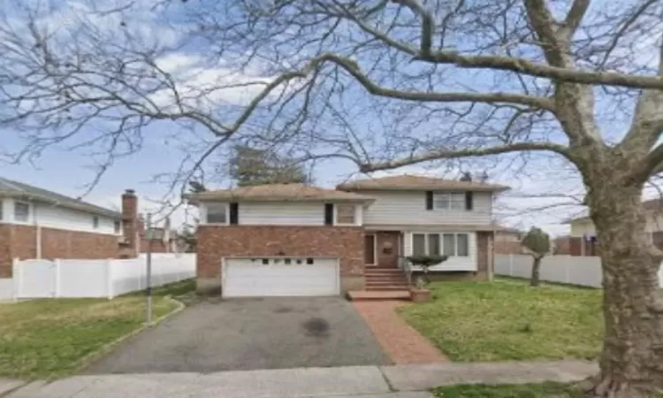 Tri-level home featuring aphalt driveway, an attached garage, fence, and a front lawn