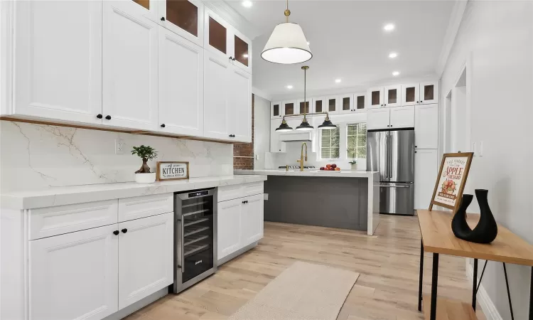 Kitchen featuring light wood finished floors, freestanding refrigerator, ornamental molding, a sink, and wine cooler