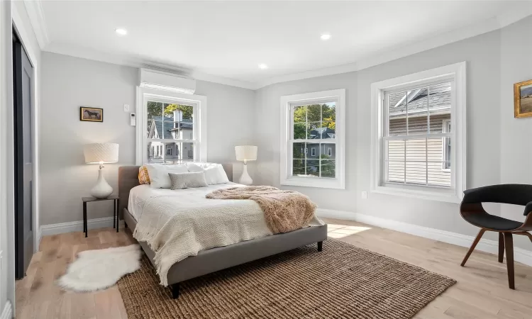 Bedroom featuring multiple windows, light wood-style floors, crown molding, and a wall mounted AC