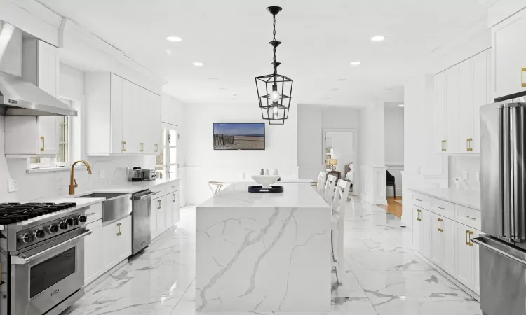 Kitchen with marble finish floor, a sink, a center island, stainless steel appliances, and wall chimney exhaust hood