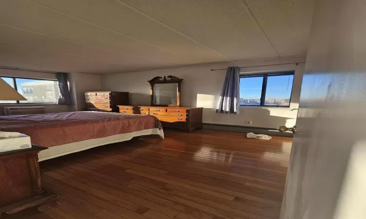 Bedroom with a wall mounted air conditioner, wood-type flooring, and baseboard heating