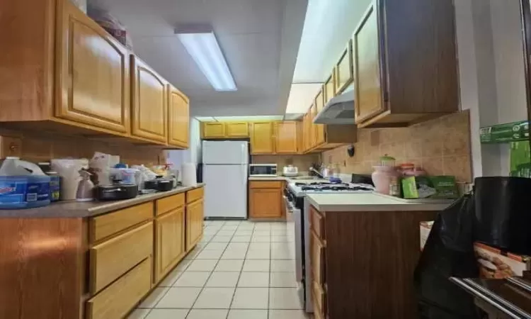 Kitchen featuring light tile patterned floors, decorative backsplash, light countertops, under cabinet range hood, and appliances with stainless steel finishes