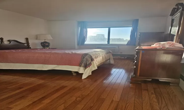 Bedroom with an AC wall unit and dark wood-style floors