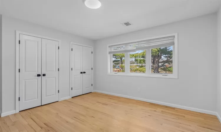 Unfurnished bedroom with baseboards, visible vents, multiple closets, and light wood-type flooring