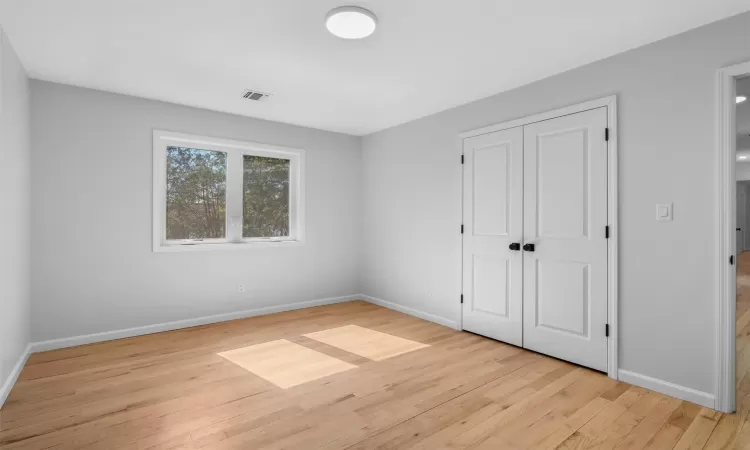 Unfurnished bedroom with a closet, baseboards, visible vents, and wood finished floors