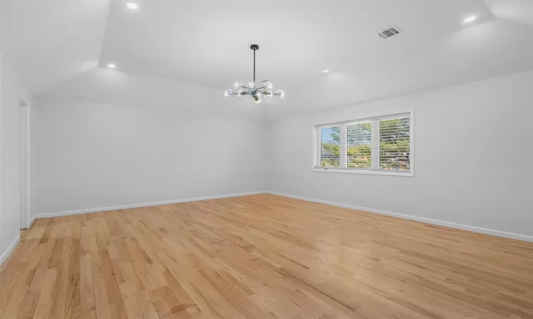 Unfurnished room with light wood finished floors, visible vents, baseboards, lofted ceiling, and a notable chandelier