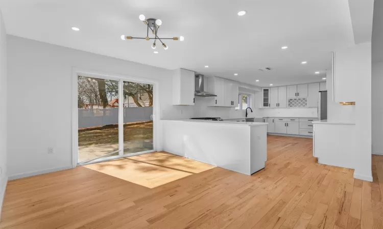 Kitchen featuring a notable chandelier, light wood-style flooring, a sink, wall chimney range hood, and light countertops