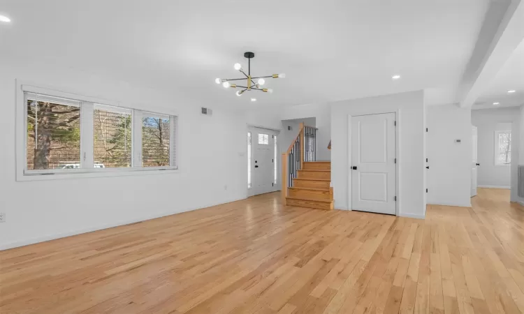 Unfurnished living room featuring baseboards, a chandelier, stairs, recessed lighting, and light wood-style flooring