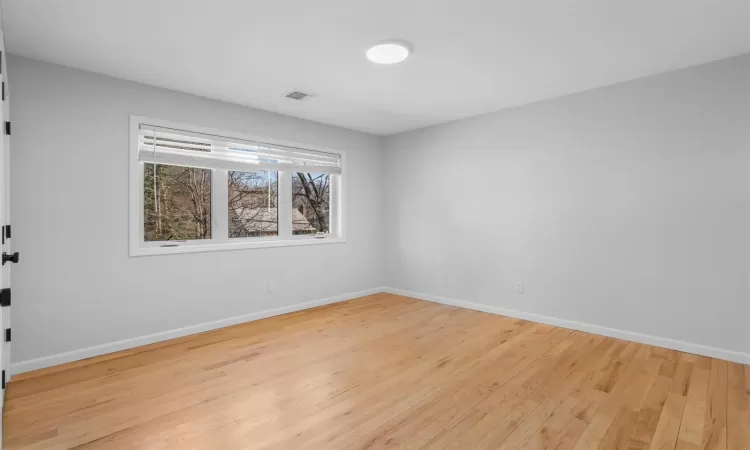 Empty room with visible vents, light wood-style floors, and baseboards