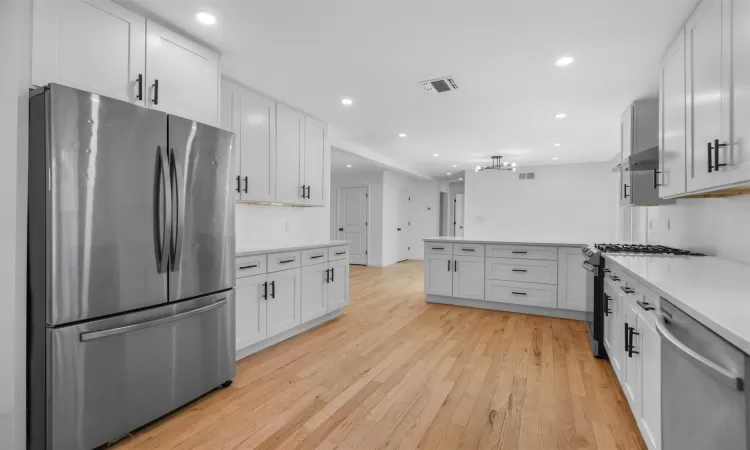 Kitchen featuring visible vents, light wood-style flooring, appliances with stainless steel finishes, light countertops, and extractor fan