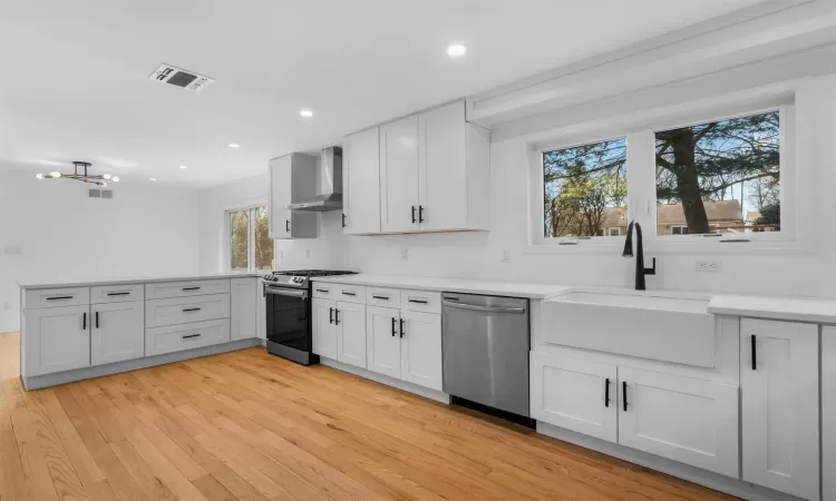 Kitchen featuring visible vents, wall chimney range hood, a peninsula, stainless steel appliances, and a sink