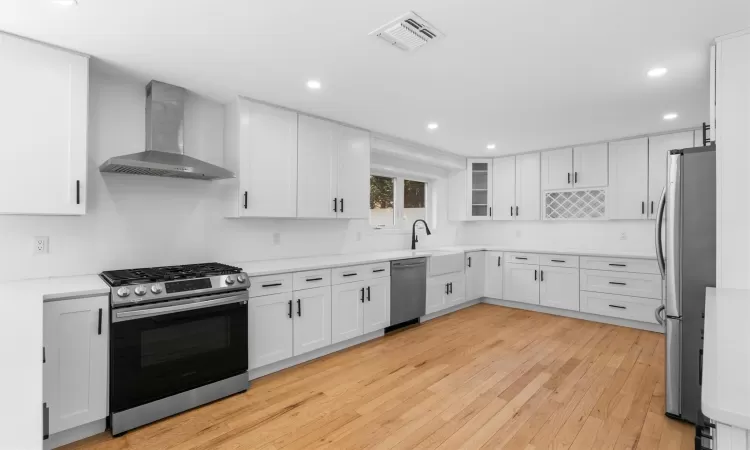 Kitchen with visible vents, light wood-style flooring, stainless steel appliances, white cabinetry, and wall chimney exhaust hood