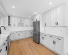 Kitchen with light wood finished floors, glass insert cabinets, white cabinets, stainless steel appliances, and a sink