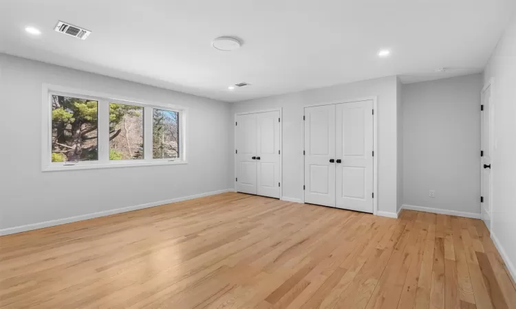 Unfurnished bedroom featuring visible vents, baseboards, two closets, and light wood finished floors