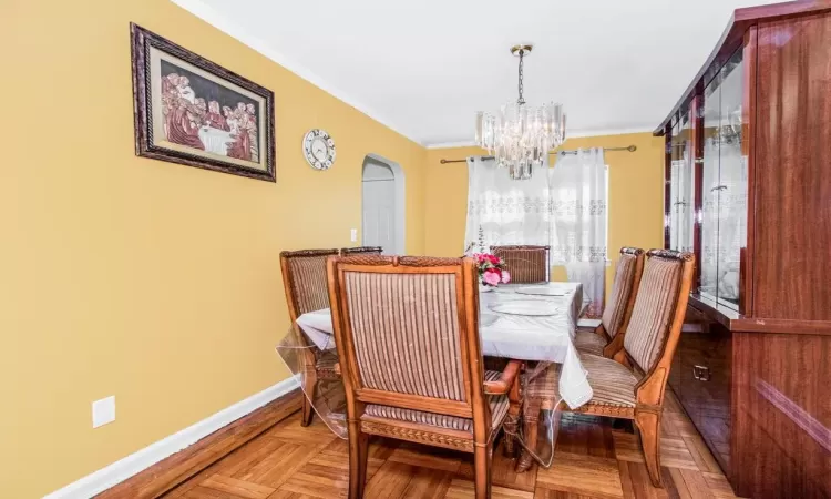 Dining room featuring crown molding, a notable chandelier, arched walkways, and baseboards