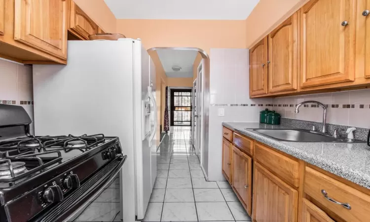 Kitchen with arched walkways, decorative backsplash, black gas stove, and a sink