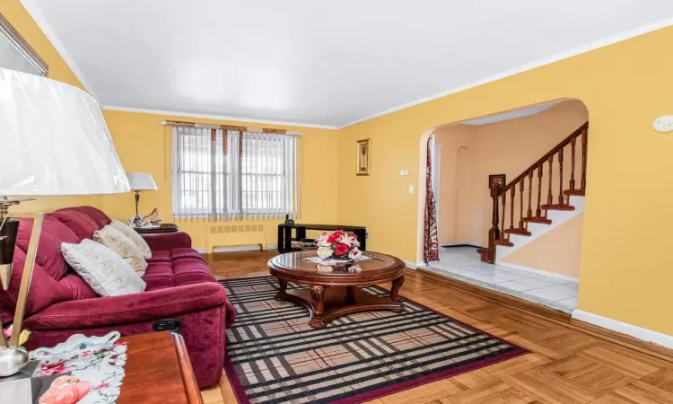 Living room with arched walkways, radiator, and crown molding