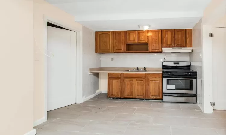 Kitchen featuring under cabinet range hood, brown cabinetry, stainless steel range with gas cooktop, and a sink