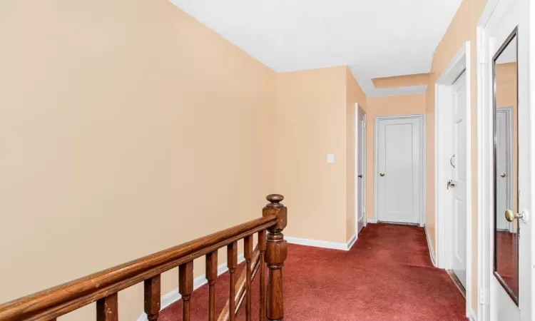 Hall with an upstairs landing, baseboards, and dark carpet