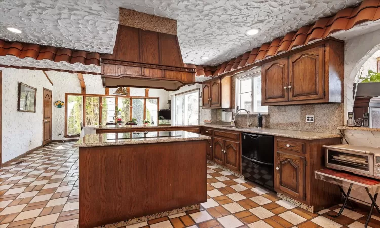 Kitchen featuring a sink, black electric cooktop, light stone countertops, and dishwashing machine