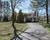 View of front of house with driveway, stone siding, a front yard, a balcony, and a chimney