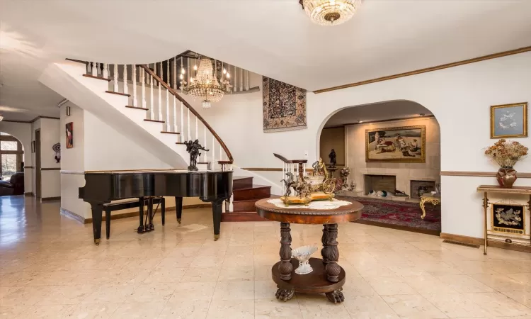 Entrance foyer with baseboards, arched walkways, a tile fireplace, stairs, and crown molding