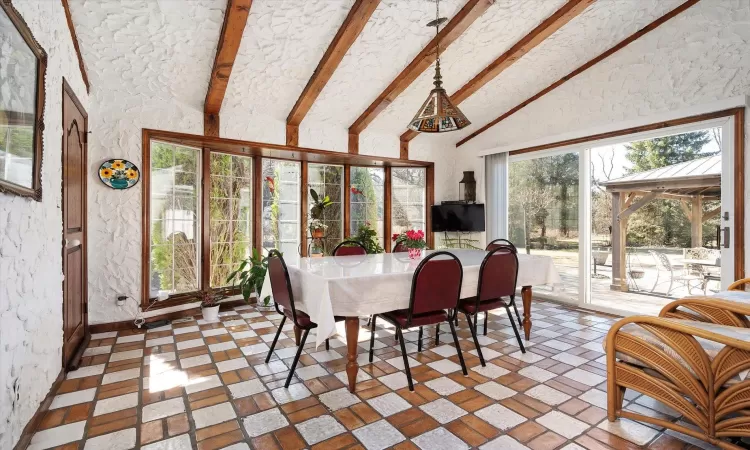 Dining room with vaulted ceiling with beams and a textured wall