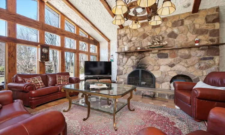 Living area with a stone fireplace, beamed ceiling, and a wealth of natural light