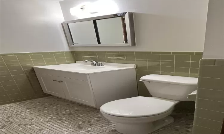 Bathroom with toilet, tile walls, vanity, and tile patterned flooring