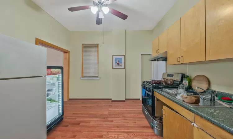 Kitchen featuring stainless steel gas range oven, a ceiling fan, under cabinet range hood, freestanding refrigerator, and light wood-style floors