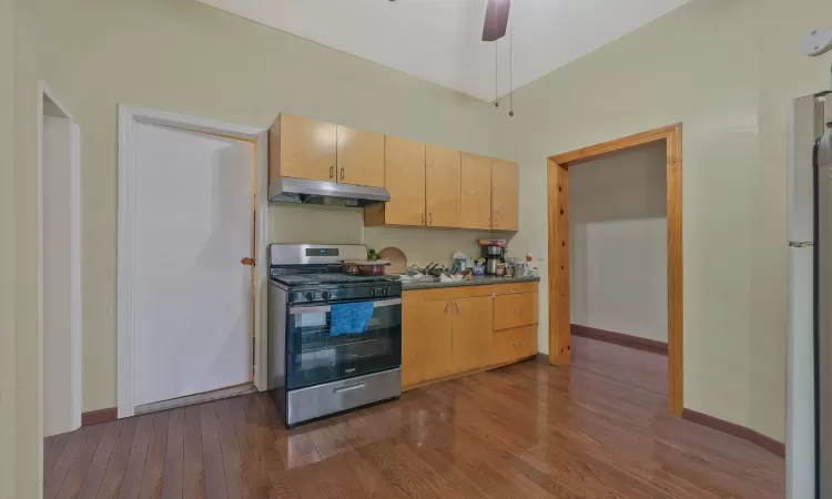 Kitchen with dark wood-type flooring, under cabinet range hood, freestanding refrigerator, stainless steel range with gas cooktop, and baseboards