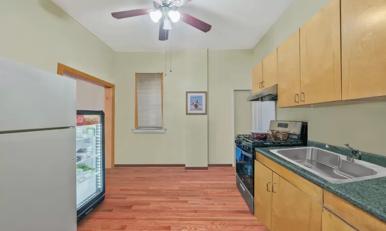 Kitchen featuring freestanding refrigerator, a sink, gas range oven, light wood-style floors, and under cabinet range hood