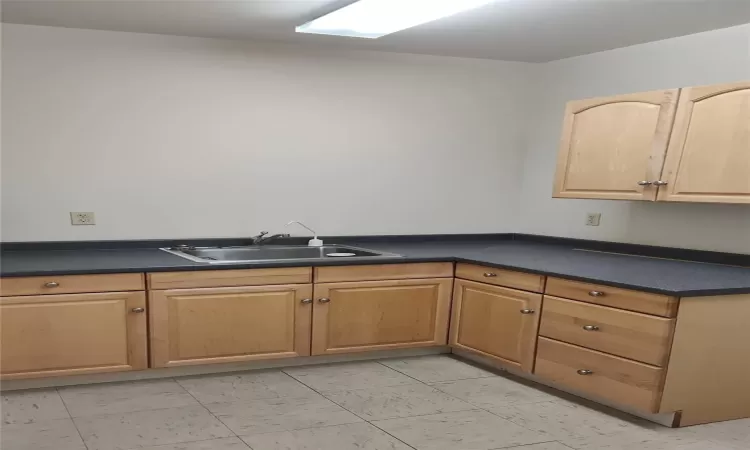 Kitchen with dark countertops, light brown cabinetry, and a sink